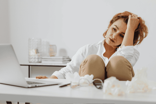 Exhausted woman in a white shirt slumped at her desk with a laptop — hypnotherapy case study of a bodyworker who released decades of chronic pain